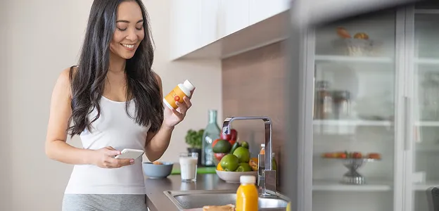 Femme souriante lisant une étiquette de complément et tenant un téléphone dans sa cuisine à Muret en Haute-Garonne 31