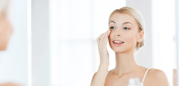 Jeune femme blonde souriante appliquant un produit sur son visage, se regardant dans un miroir à Muret en Haute-Garonne 31